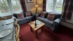 Una sala de estar acogedora con dos sofás grises, una mesa de centro de madera y una mesa de comedor preparada para cuatro.