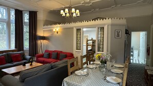 A dining area with a long table set for four, a red sofa, and a chandelier. - Cosy self catering apartment in large Victorian Residence (Buxton)