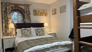 A bedroom with a bed, two bedside tables, a lamp, floral curtains, a window with a view, and a wooden ladder. - Cosy self catering apartment in large Victorian Residence (Buxton)