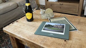 Une bouteille de Prosecco, deux verres, un livre d’or et une télécommande sur une table en bois dans un salon.
