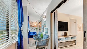 A modern living room with a blue sofa, wicker chairs, a TV, and a fireplace. - Penthouse/Oceanfront Building w/ Beach Access+ Heated Pool/Sunset & Rocket Views (Ormond Beach)