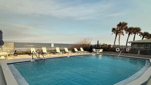 A rectangular swimming pool with a tiled edge, surrounded by lounge chairs and a fence. - Penthouse/Oceanfront Building w/ Beach Access+ Heated Pool/Sunset & Rocket Views (Ormond Beach)