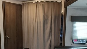 Kompakti matkailuajoneuvon sisustus, jossa on puuovi, verhoilla varustettu ikkuna, pieni oleskelualue ja pieni keittiö.