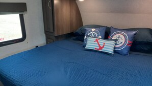 Sängyssä on sininen, kuvioitu päiväpeite, kaksi meriaihekuvioitua koristetyynyä ja ikkunasta avautuu näkymä ulos.