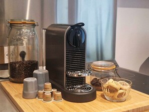 A coffee maker, a glass jar with coffee beans, and a glass container with coffee pods on a wooden surface.