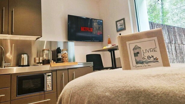 A modern kitchen with a microwave, oven, and a coffee maker. A television displaying the Netflix logo is mounted on the wall.