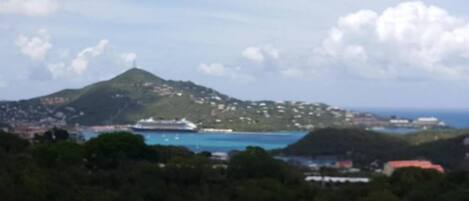 A coastal landscape with a prominent hill, a body of water, and a cruise ship.