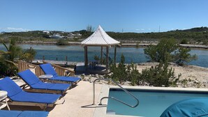 Zona de piscina con sillones de descanso, un pabellón y vistas al agua.