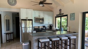 Una cocina moderna con armarios blancos, electrodomésticos de acero inoxidable, una isla grande con taburetes y un ventilador de techo.