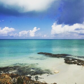 A beach with clear turquoise water, white sand, and rocky outcrops.