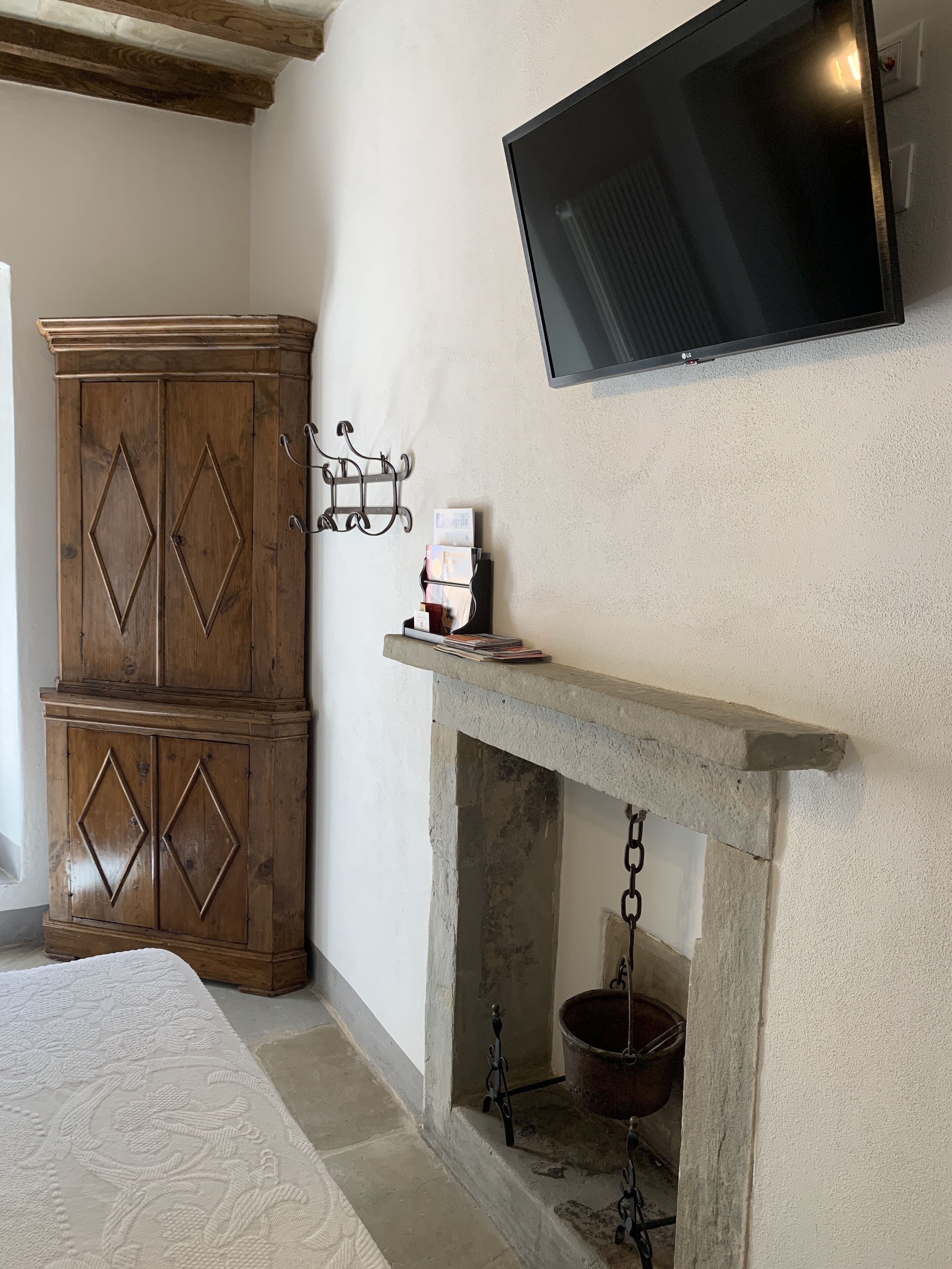 A bedroom with a wooden wardrobe, a mounted TV, and a fireplace with a stone mantle.