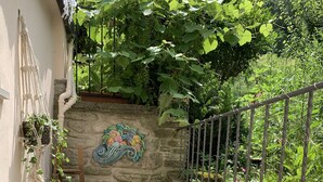 A wooden bench and table set against a stone wall with a decorative mural, surrounded by lush greenery.