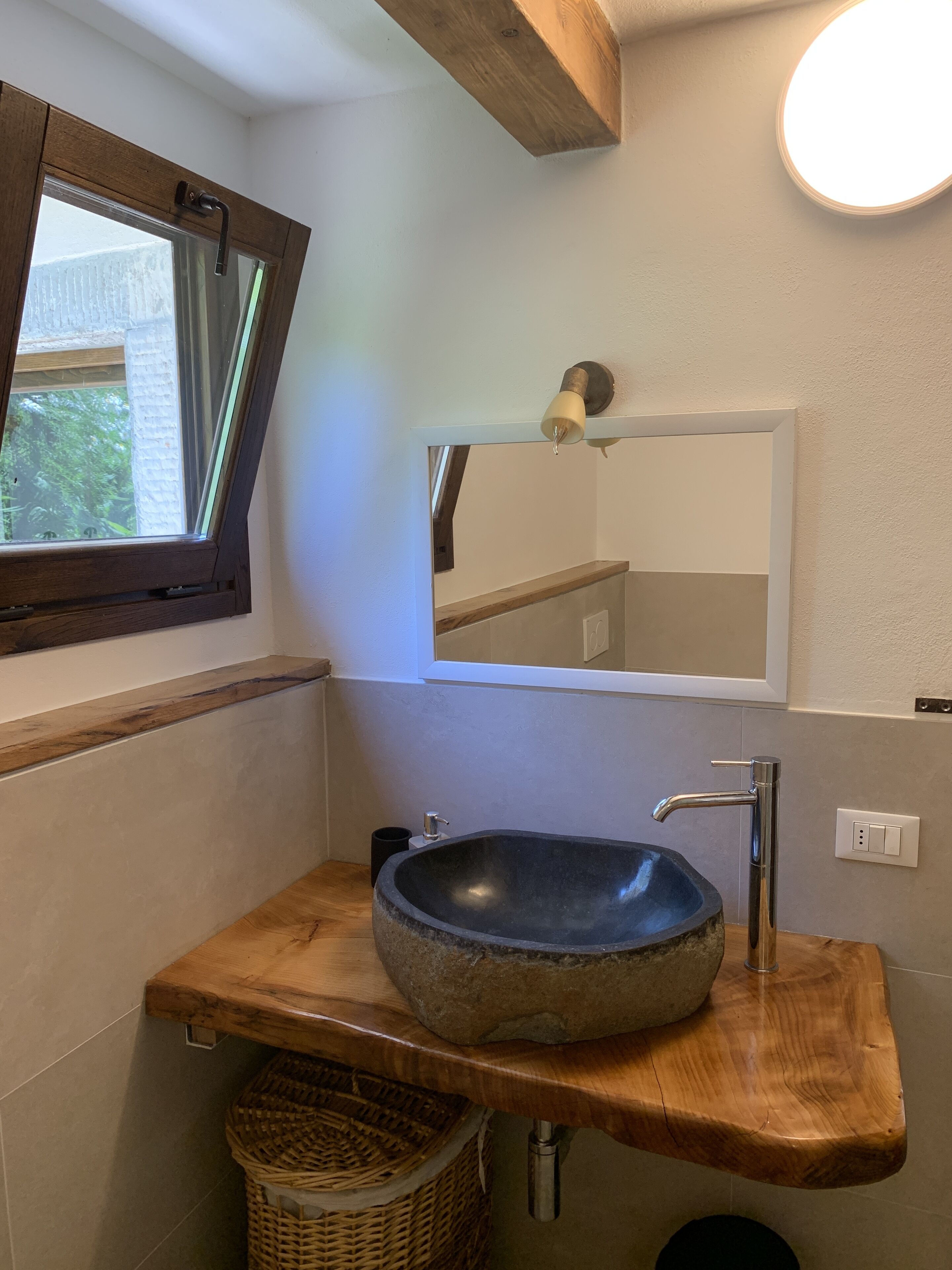 A bathroom with a wooden vanity, a stone sink, a mirror, and a window with a view of greenery.