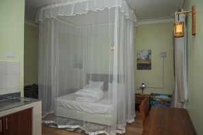 A room with a bed under a mosquito net, a desk with a lamp, and a painting on the wall. - Mt. Rwenzori Golf Resort & Spa (Fort Portal)