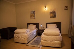 A hotel room with two single beds, a nightstand with a lamp, a dark armchair, and two wall-mounted artworks. - Mt. Rwenzori Golf Resort & Spa (Fort Portal)