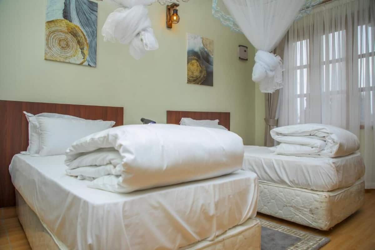 A hotel room with two beds, a wooden headboard, a large window with sheer curtains, and wall art.
