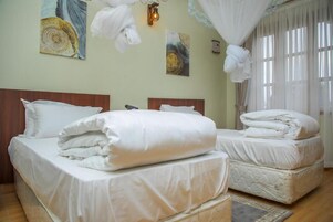 Habitación de hotel con dos camas, cabecero de madera, ventana grande con cortinas translúcidas y decoración en la pared.