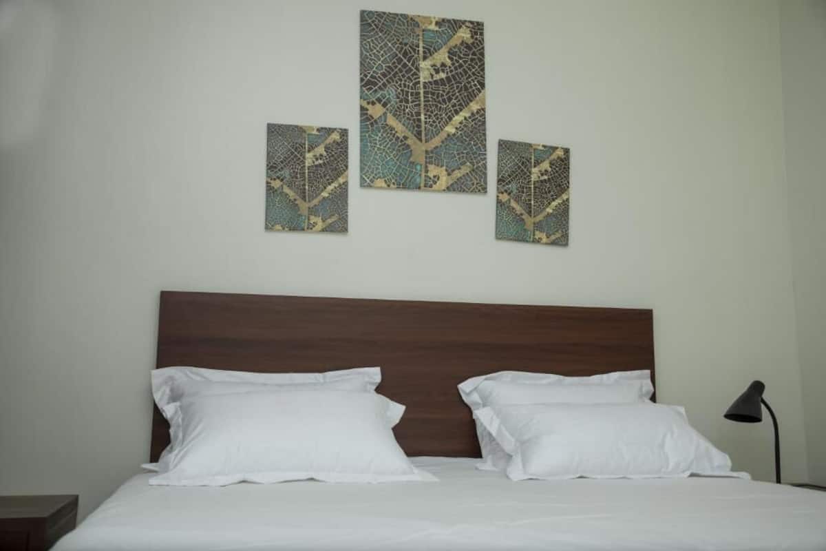 A neatly made bed with white linens and two pillows, a wooden headboard, and a wall-mounted artwork above.