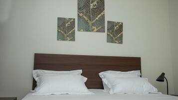 Una cama bien tendida con sábanas blancas y dos almohadas, un cabecero de madera y una obra de arte colgada en la pared.