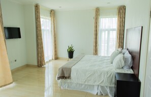A bedroom with a bed, a TV mounted on the wall, and a potted plant.