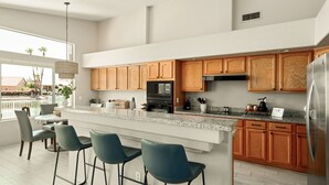 Cozinha moderna com armários de madeira, geladeira de aço inoxidável e um espaço bar com banquetas.