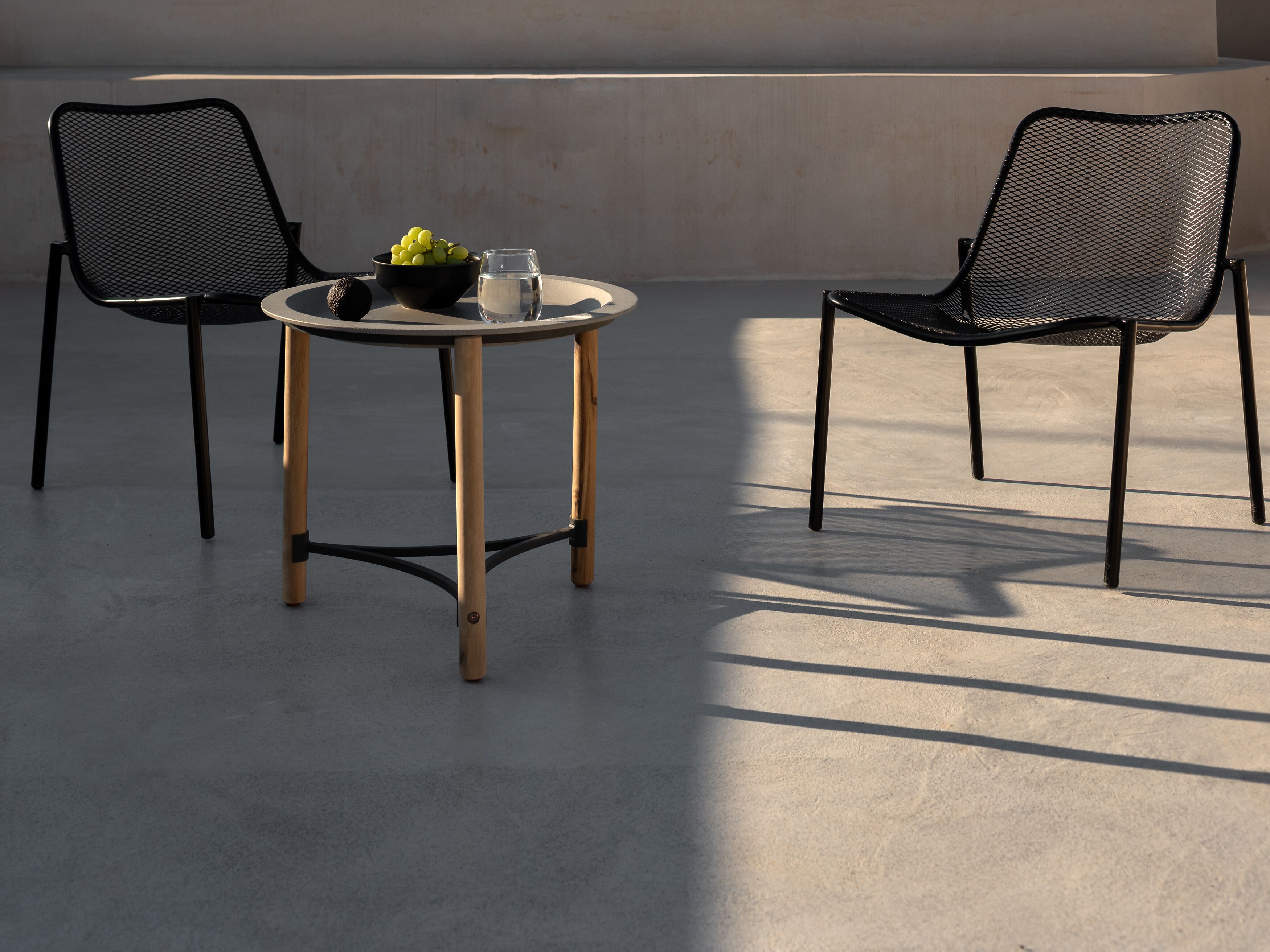A round table with two chairs, a bowl of fruit, and a glass of water.