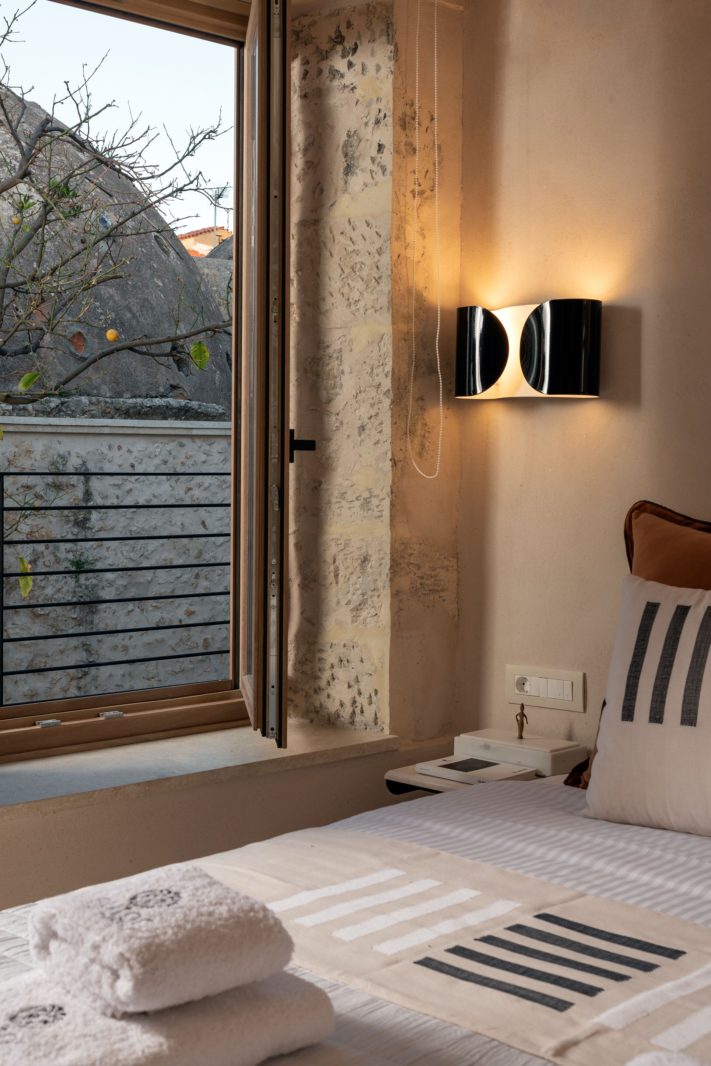 Une chambre avec une grande fenêtre, une table de chevet avec une lampe et un lit agrémenté d’oreillers à rayures.