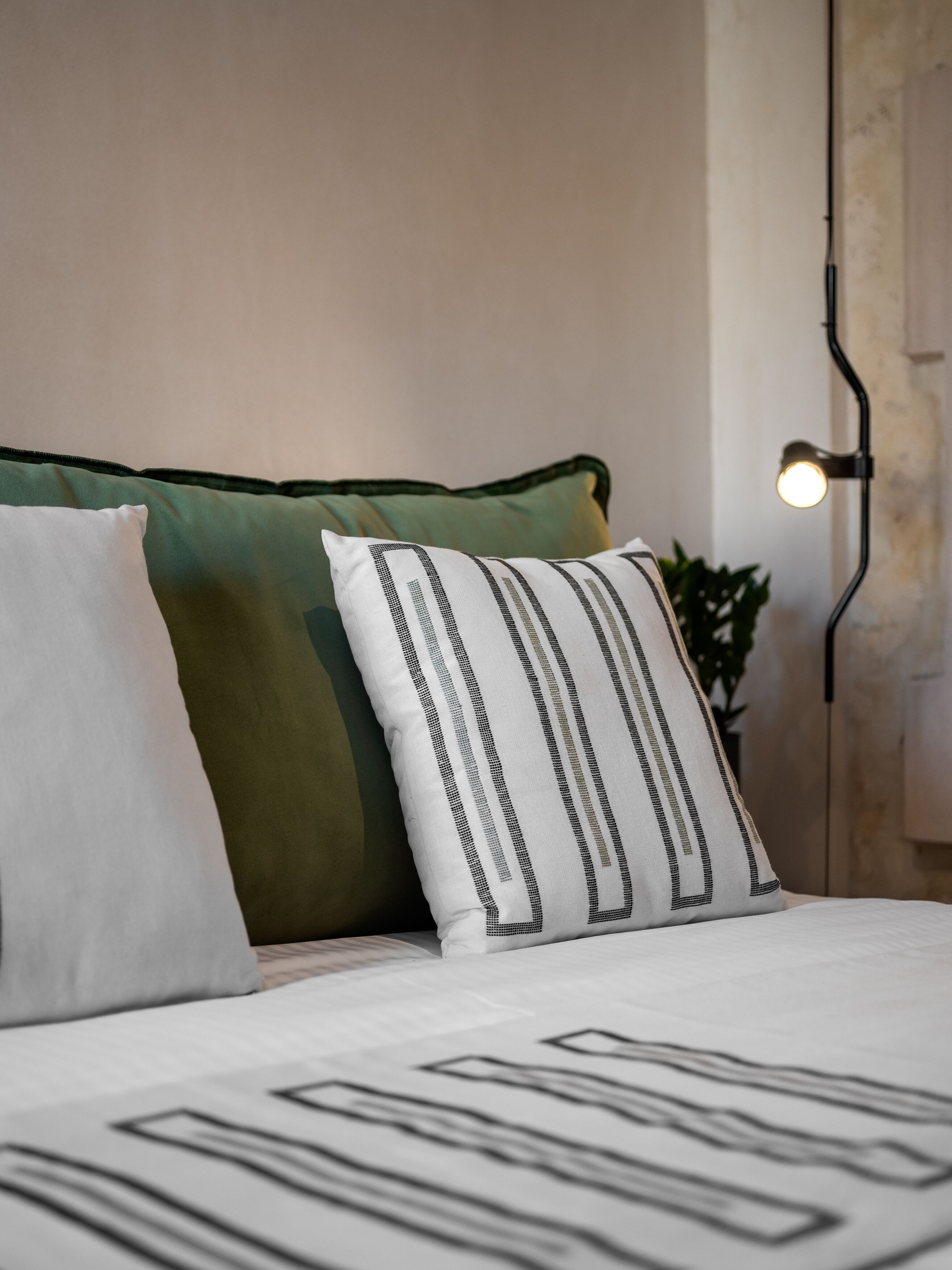 A bed with a white and green pillow, a black and white striped pillow, and a white bedspread with black lines.