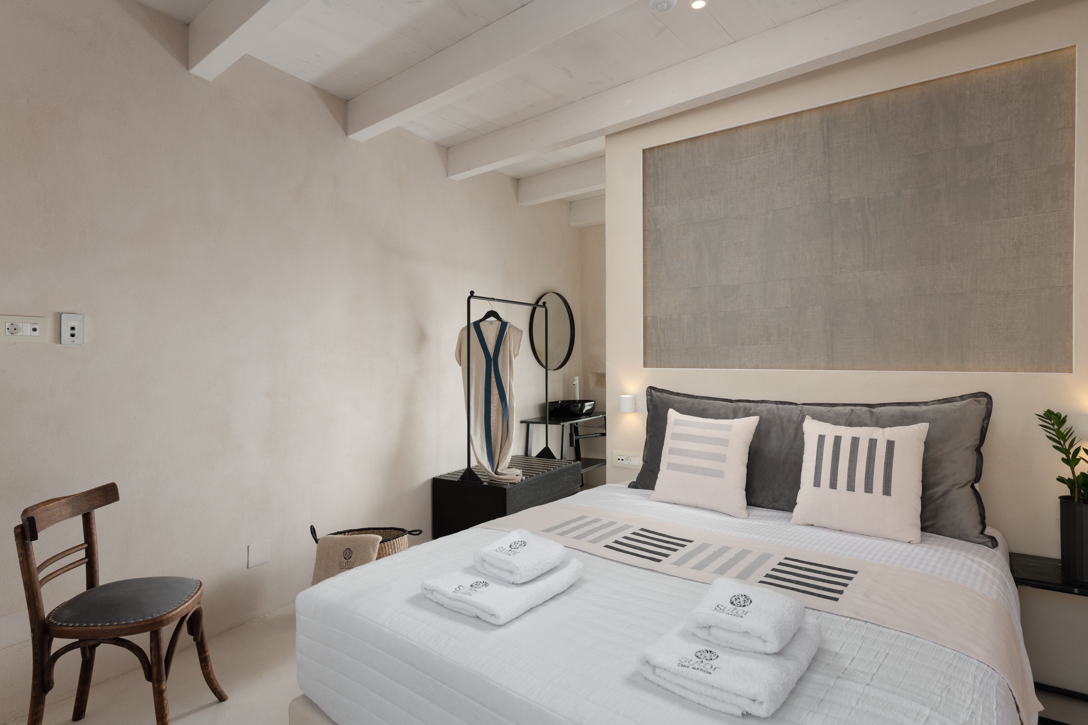 Ein modernes Schlafzimmer mit einem großen Bett, einem Holzsessel, einem Nachttisch und einem an der Wand befestigten Kleiderständer.