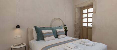 A neatly made bed with a striped bedspread, a small bedside table with a lamp, and a potted plant on the nightstand.