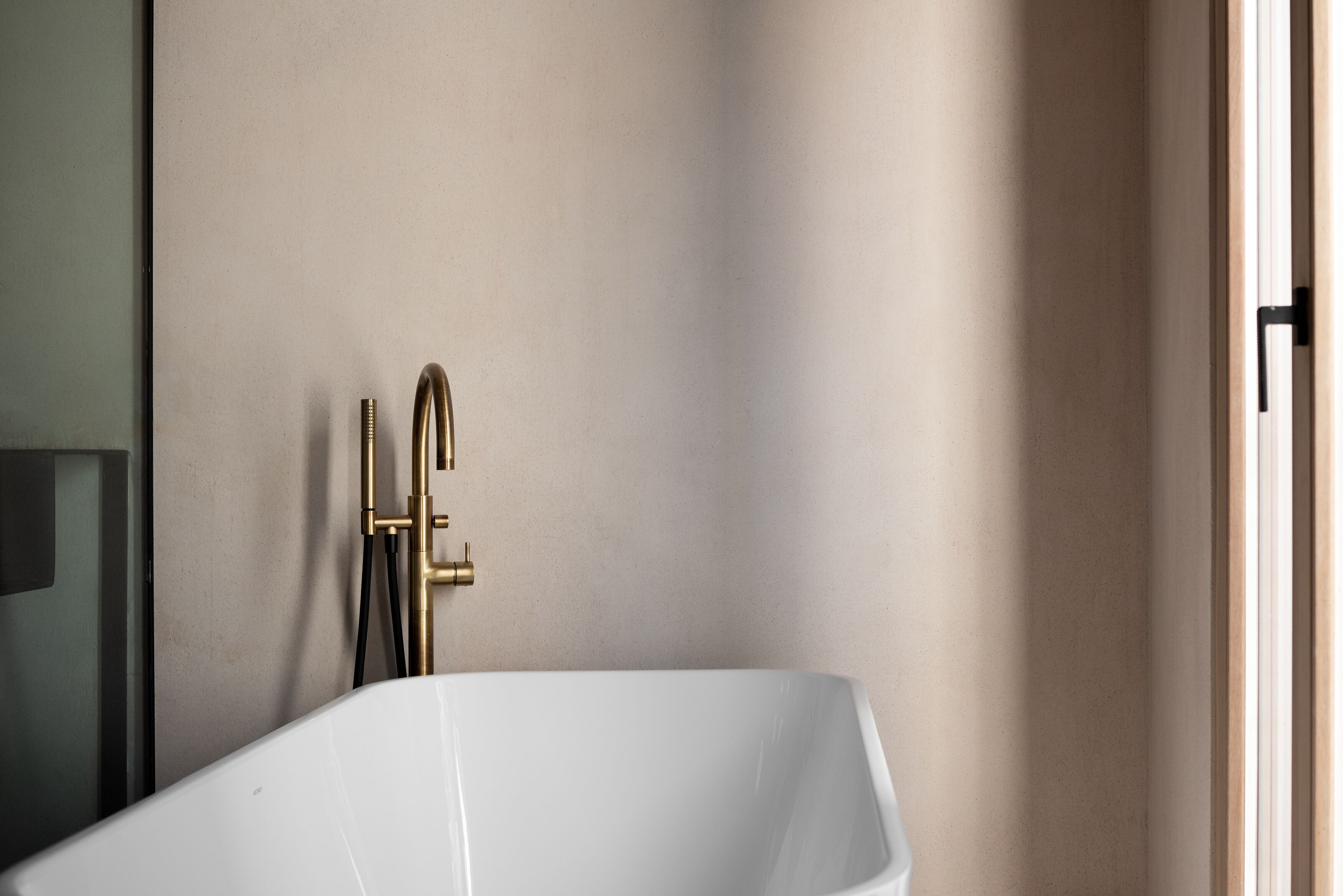 A modern bathroom with a freestanding bathtub, a gold faucet, and a visible showerhead.