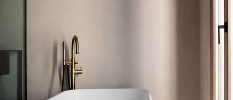 A modern bathroom with a freestanding bathtub, a gold faucet, and a visible showerhead.