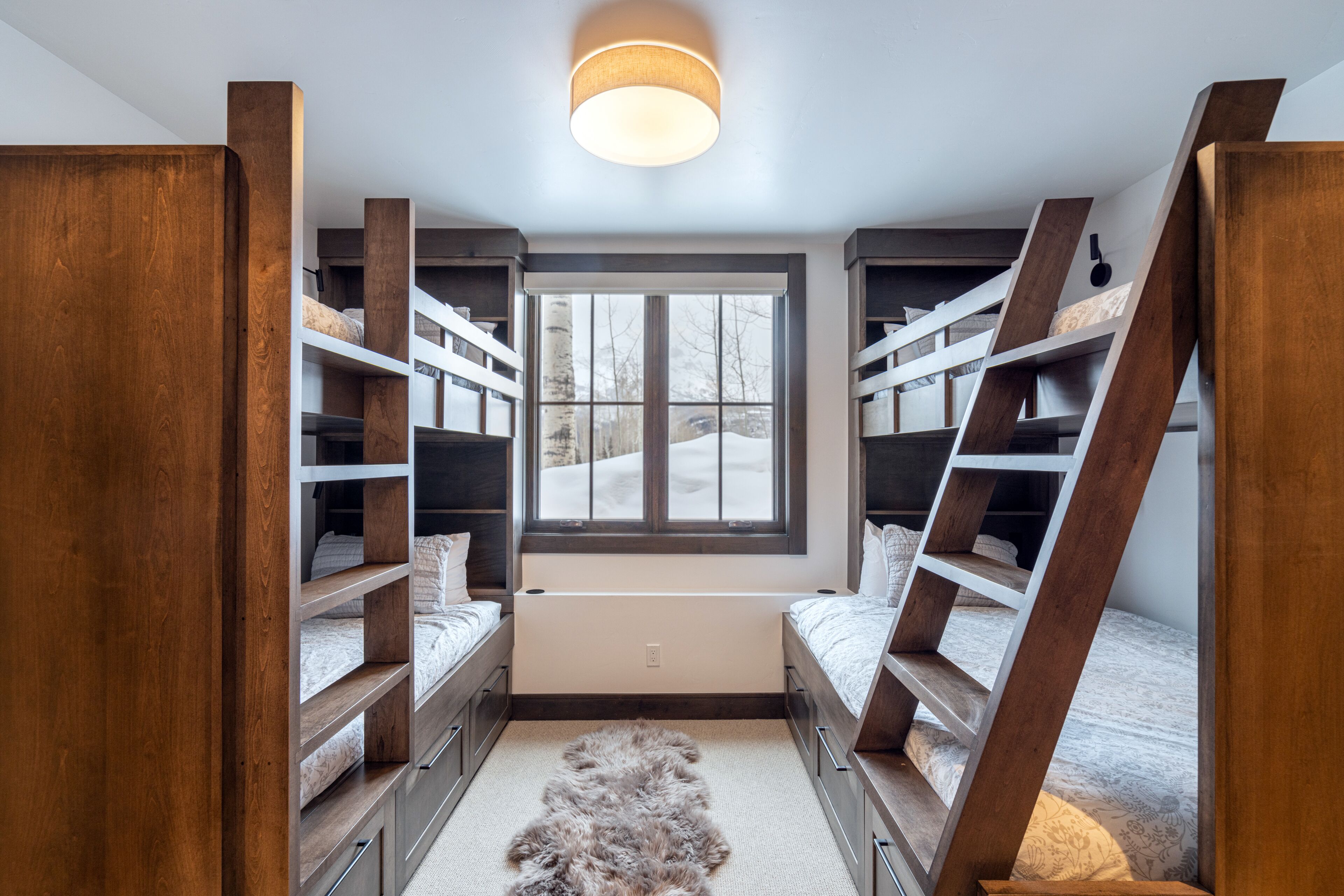 Une chambre avec deux lits superposés, des étagères en bois, une grande fenêtre et un tapis en fourrure.