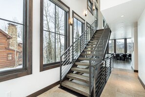 Un intérieur moderne avec un escalier en bois, de grandes fenêtres et un coin repas.