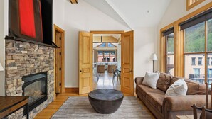 A spacious living room with a stone fireplace, a large window, and a view of the city.