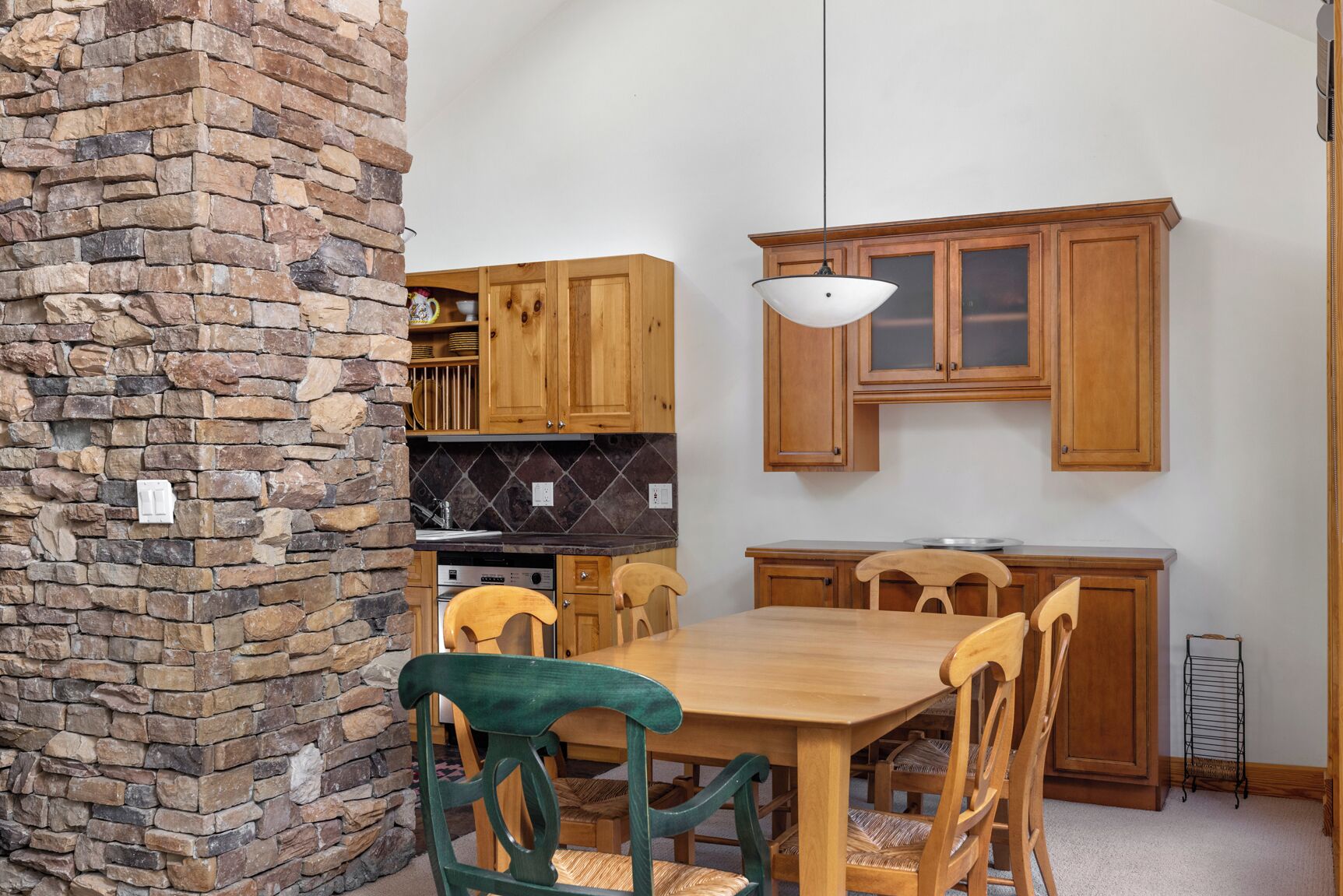 A dining area with a stone wall, wooden cabinets, a wooden table, and chairs.