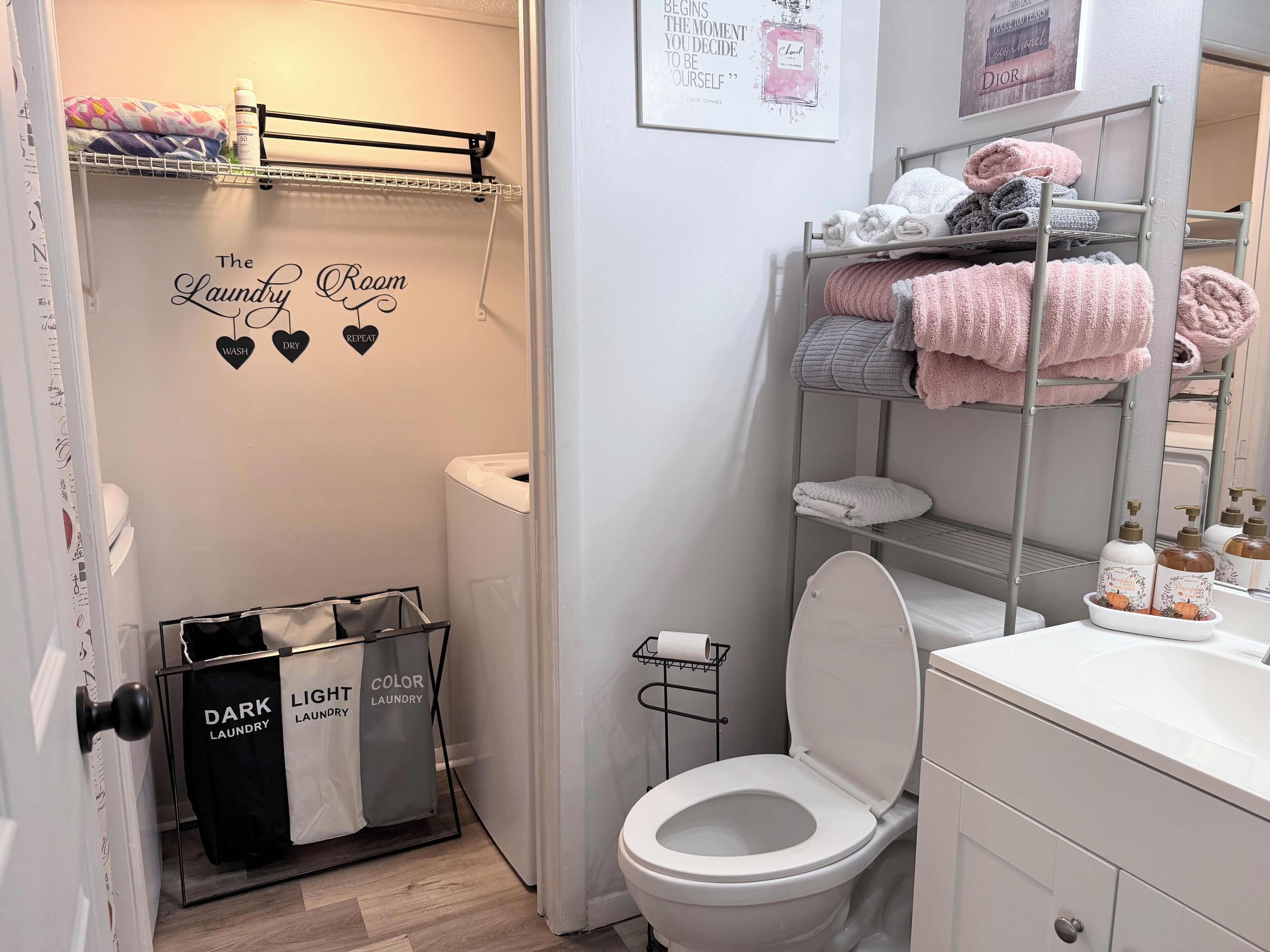 Un baño moderno con un inodoro, un estante con toallas ordenadas, un estante con botellas y una pared con una cita inspiradora.