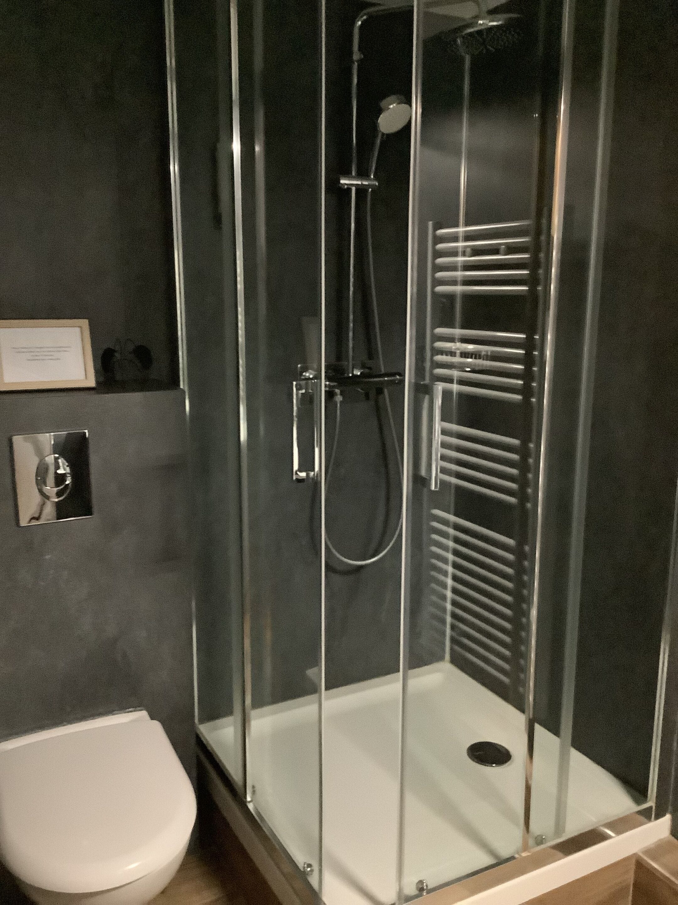 A glass-enclosed shower stall with a handheld showerhead and a handheld shower attachment.
