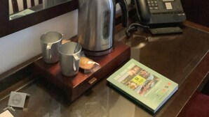 Una habitación de hotel con una mesa de madera, una tetera, dos tazas, un teléfono y una revista.