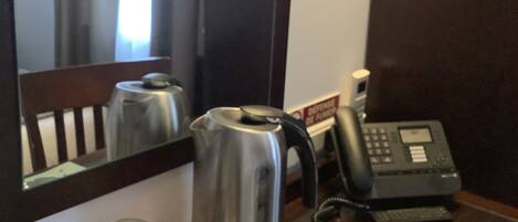 A hotel room with a wooden table, a kettle, two mugs, a telephone, and a magazine.