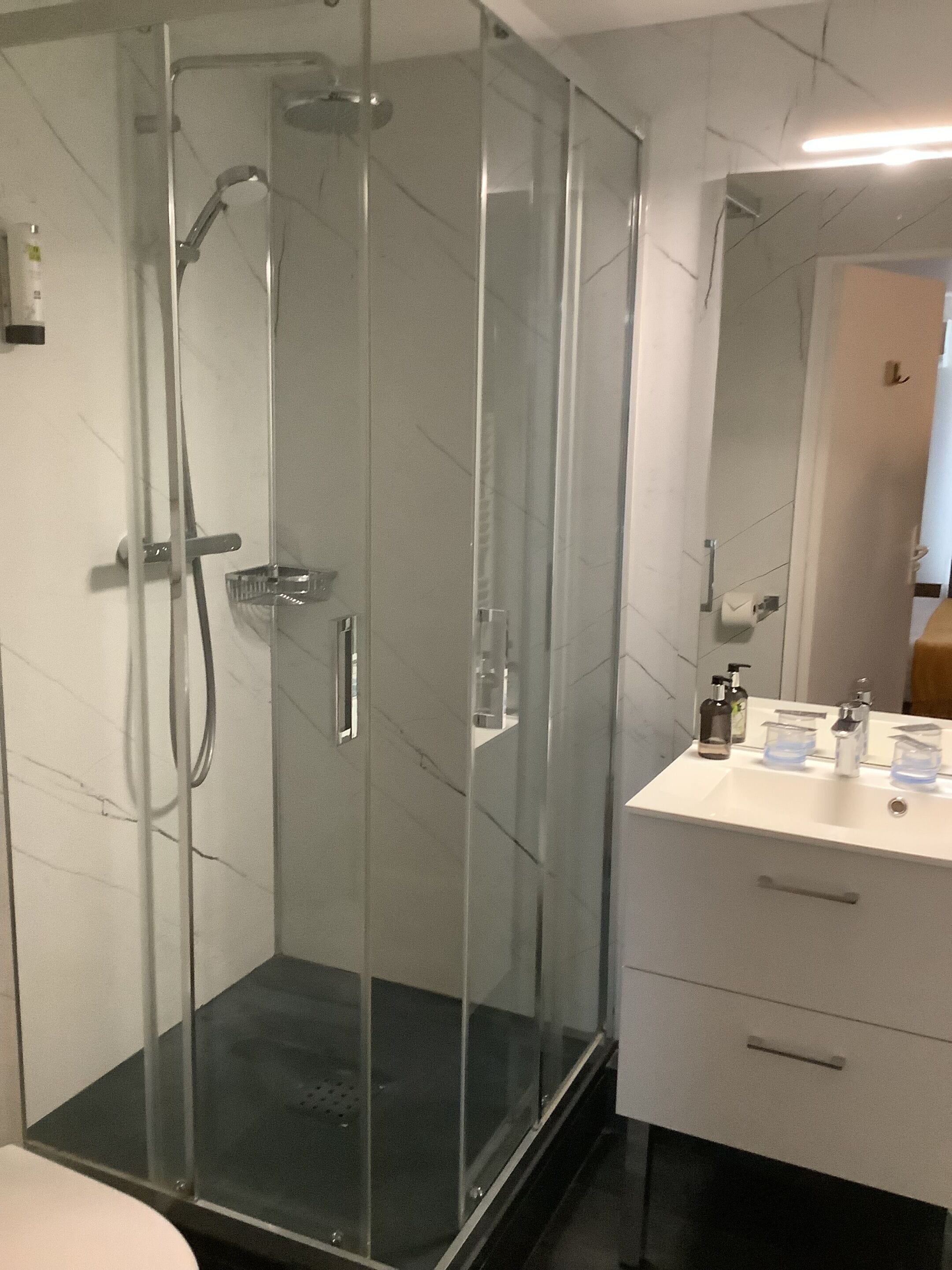 A modern bathroom with a glass-enclosed shower, a white sink with a mirror, and a black countertop.