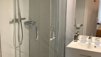 Un baño moderno con ducha envuelta en cristal, un lavabo blanco con espejo y encimera negra.