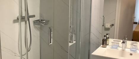 Un baño moderno con ducha envuelta en cristal, un lavabo blanco con espejo y encimera negra.