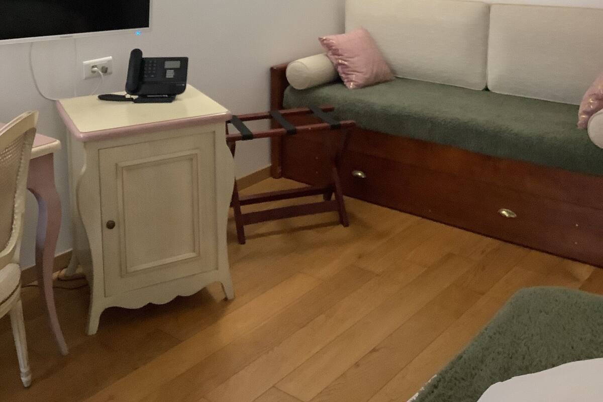 Ein kleiner, gemütlicher Raum mit Schreibtisch, Stuhl und einem Bett mit Kissen.