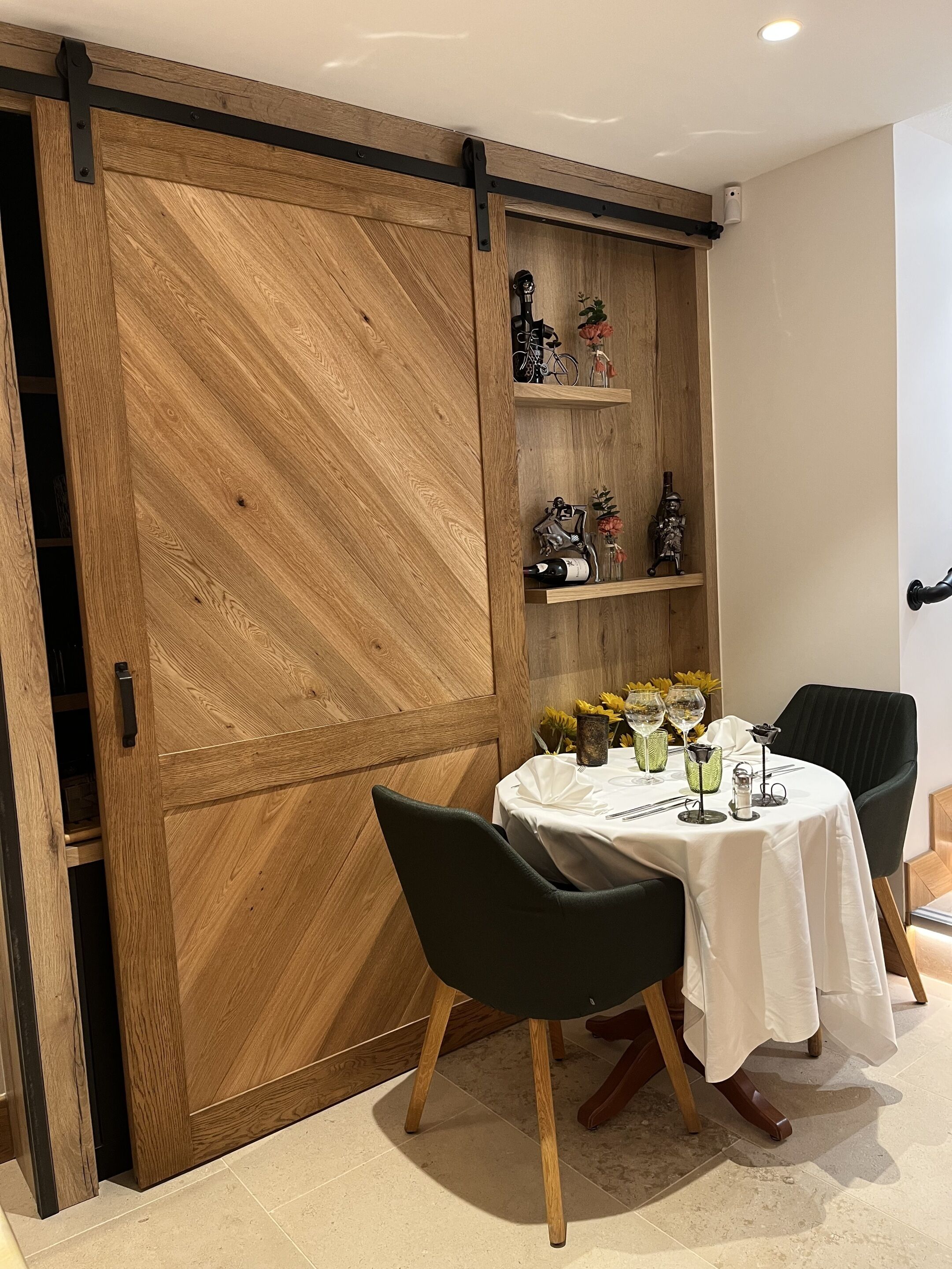 A dining area with a wooden sliding door, a table set with white tablecloth, green chairs, and decorative items on shelves.