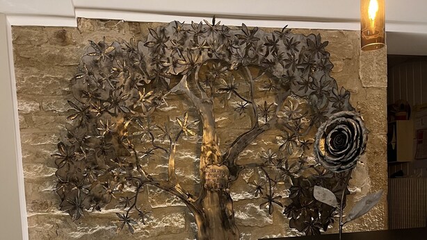 Una escultura de árbol montada en la pared, con un fondo de piedra texturizada, una encimera de madera a la derecha y una mesa con cubiertos al frente.