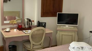 Habitación de hotel con cama, escritorio con computadora, silla, lámpara de escritorio, teléfono y un cesto de basura pequeño.