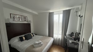 Habitación de hotel con cama, escritorio, silla, lámpara y ventana con cortinas.