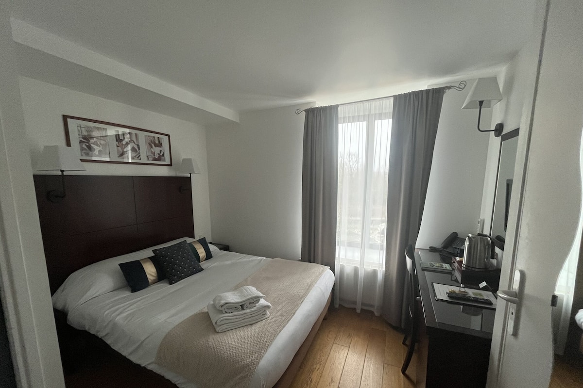 Ein Hotelzimmer mit Bett, Schreibtisch, Stuhl, Lampe und einem Fenster mit Vorhängen.