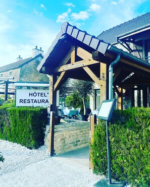 Ein Hotel mit Eingangsbereich, einer überdachten Terrasse und einer Steinsäule, die zum Eingang führt. Auf dem Schild steht 'Hôtel Restaura'.